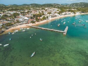Aerial view of Armação dos Búzios pier and coastline with boats in turquoise waters.