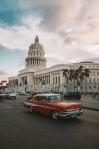 A classic car drives past the historic El Capitolio in Havana, Cuba, under a dramatic sky.